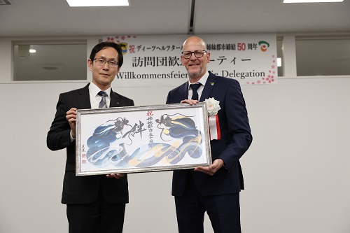交流の継続を願って贈られた記念品の一筆龍を手にする両市長
